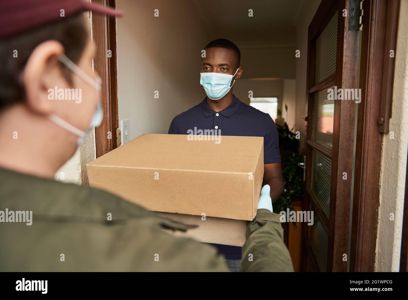 African man in a mask receiving a courier package at home Stock Photo