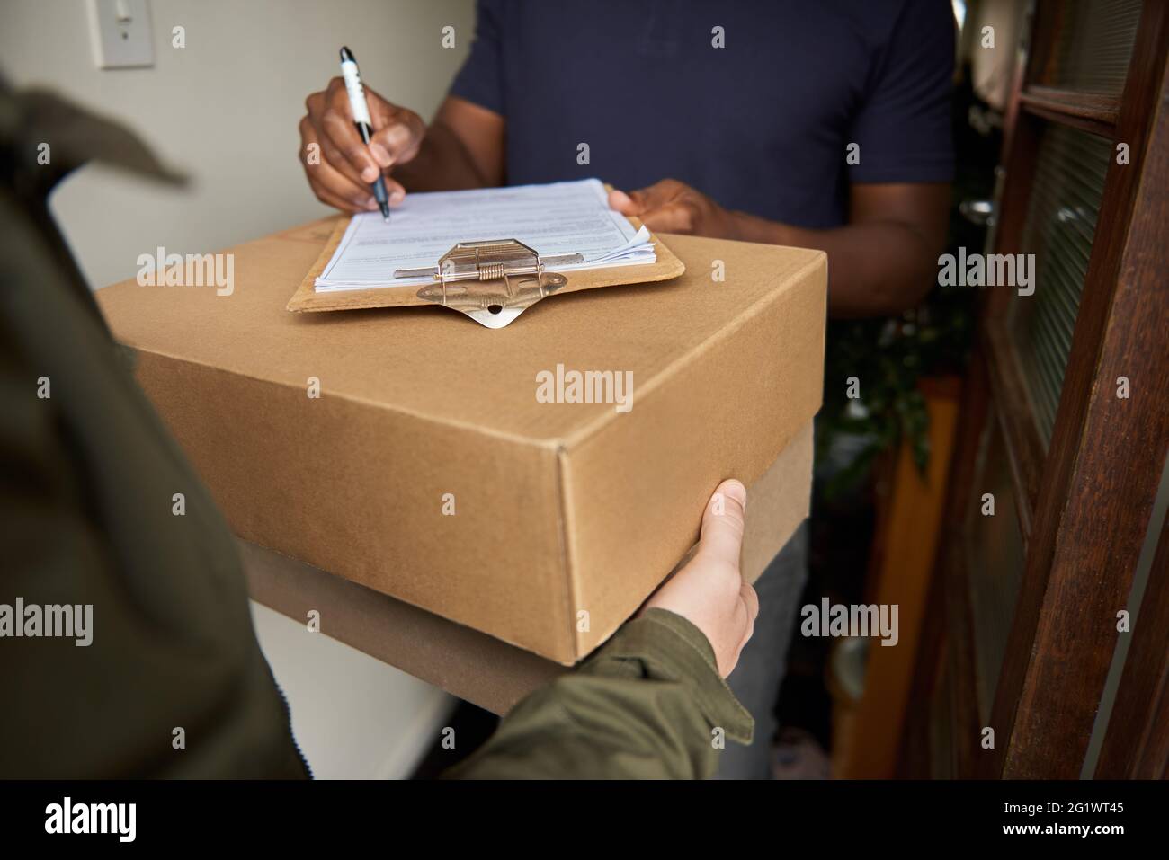 African man signing a courier's clipboard to receive a package Stock Photo