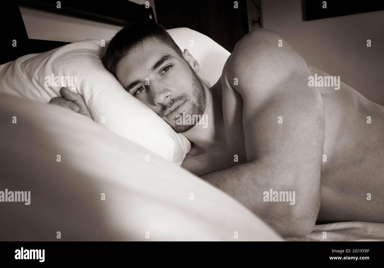 Good looking naked man with defined muscular body in bed, looking at camera Stock Photo