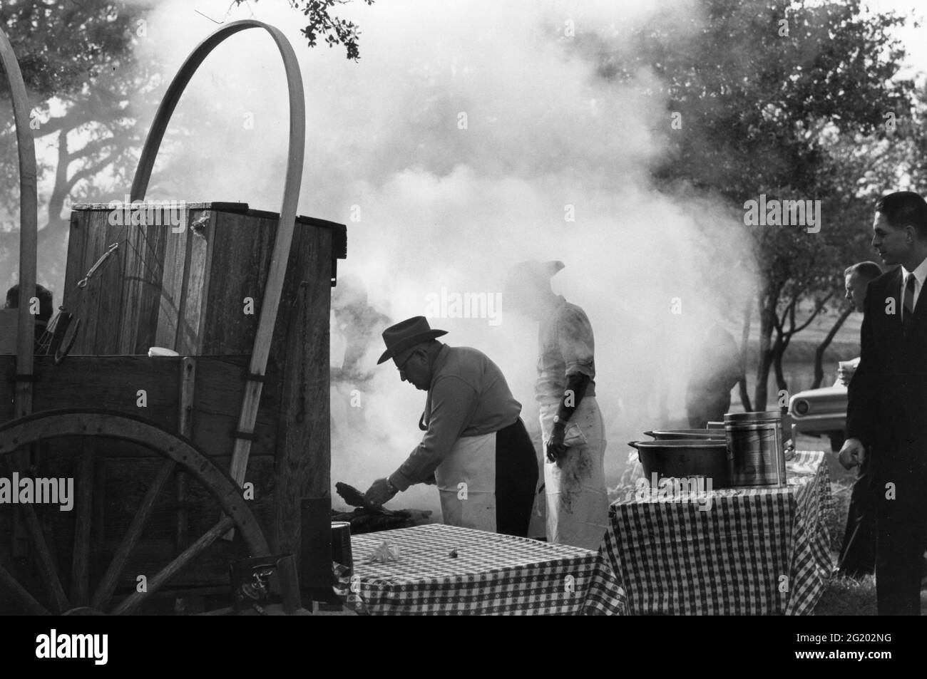 Reporters (right) wait their turn for barbecue being prepared at President Lyndon B Johnson's Texas ranch for West German Chancellor Ludwig Erhard, Johnson City, TX, December 1963. (Photo by Yoichi Okamoto/White House Photo Collection/RBM Vintage Images) Stock Photo