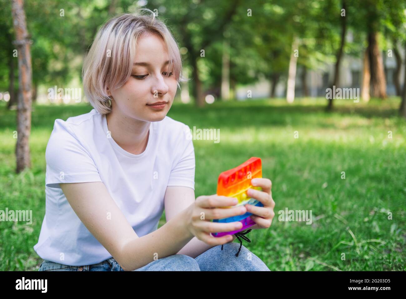 Teen girl sits in a park near campus and plays pop it Stock Photo