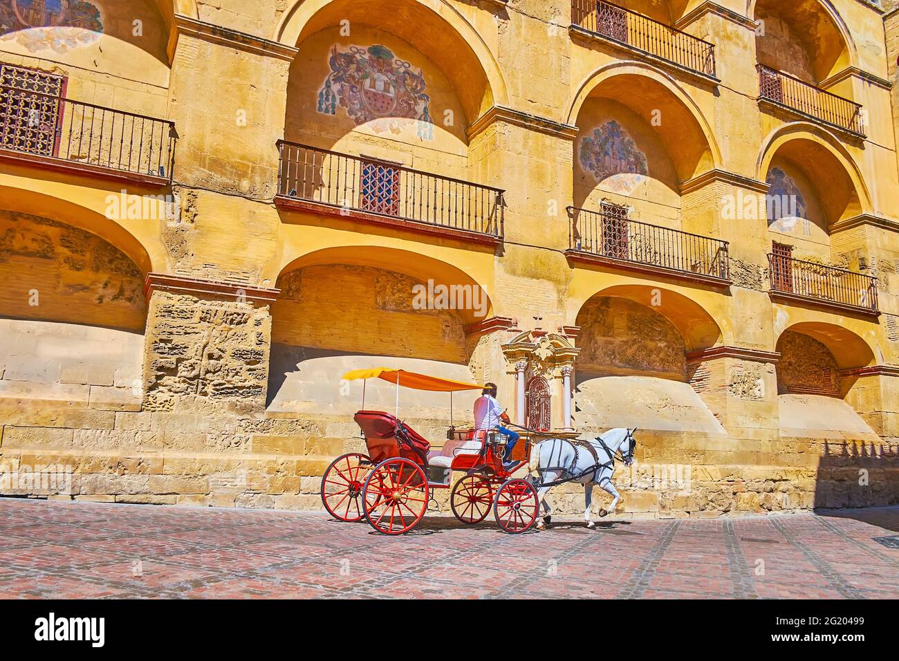 The vintage horse drawn carriage rides along the medieval wall of Mezquita-Catedral, decorated with niches and emblems, Cordoba, Spain Stock Photo