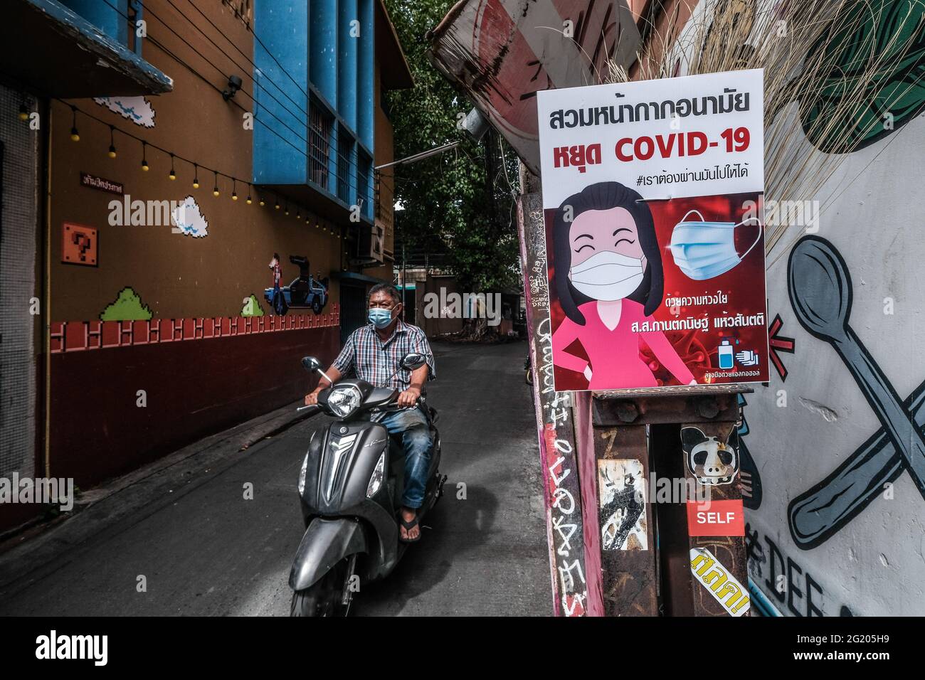 Covid 19 signage attached to a lampost at the entrance to a narrow alley in Talat Noi, Bangkok, Thailand Stock Photo