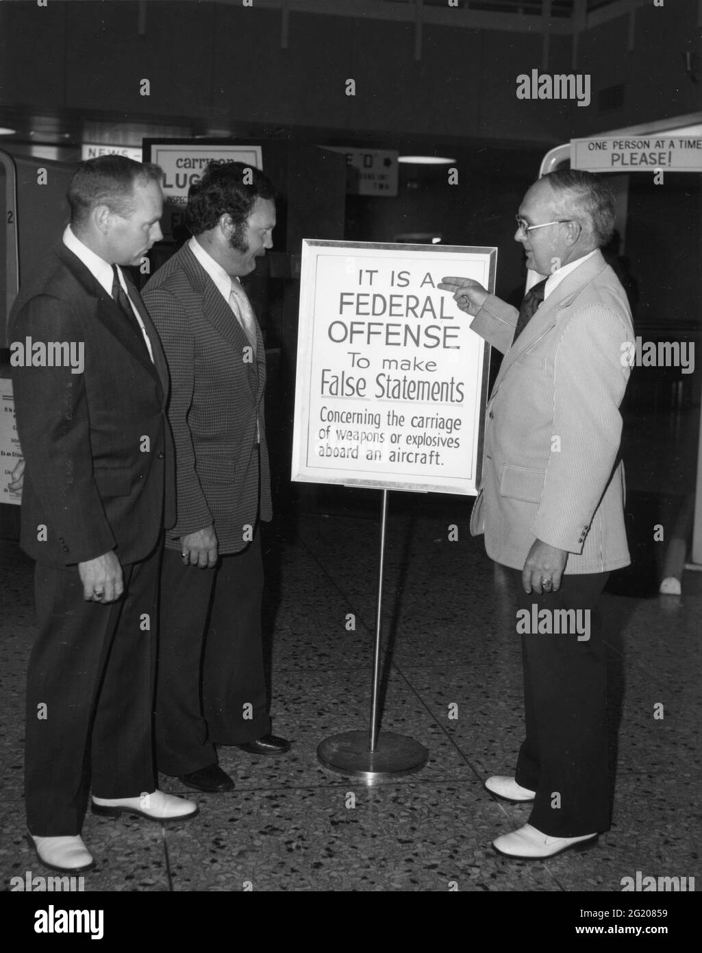 Airport officials view new signage warning passengers of penalties for making false statements regarding hijacking or carrying weapons aboard an aircraft, no location, 1970. (Photo by Federal Aviation Administration/RBM Vintage Images) Stock Photo