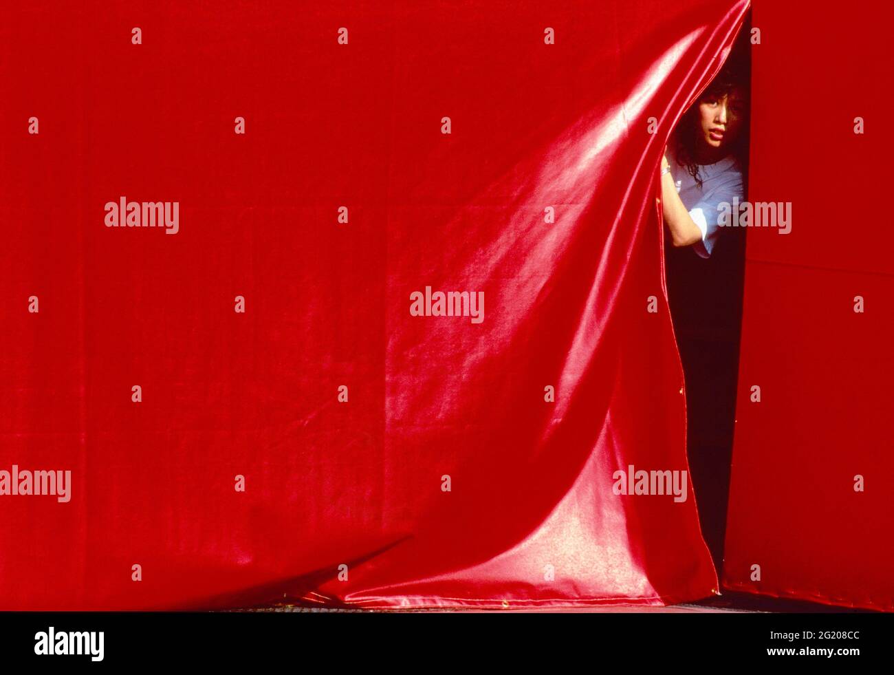 Asian girl peeking through the red curtain, 1993 Stock Photo