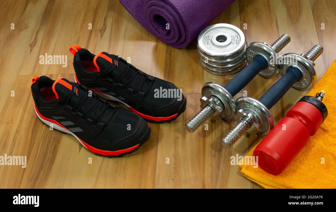 Gym set of pair of black sports shoes, exercise weights, yellow towel and red bottle with water on wooden floor Stock Photo