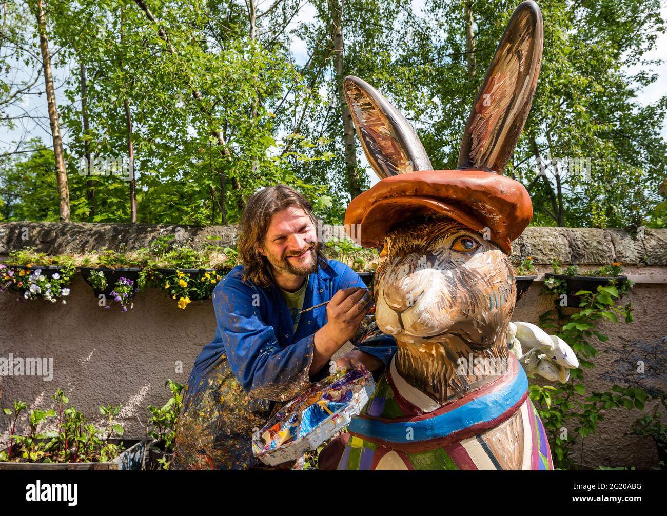 Artist Chris Rutterford paints a humorous giant fibreglass hare sculpture in his outdoor studio for a charity art trail, Scotland, UK Stock Photo