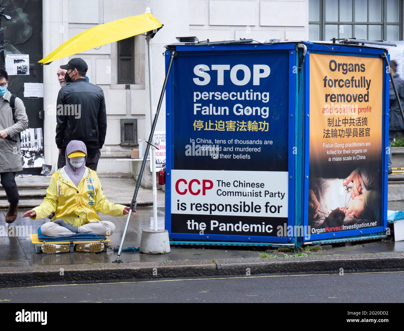 A cross legged  Falun Gong practitioner protests at  Rally outside the Chinese Embassy in London UK,  marking the 32nd anniversary of the  June 4th massacre at Tiananmen Square, China. With posters reading, Stop persecuting Falun Gong and Organs forcefully removed Stock Photo