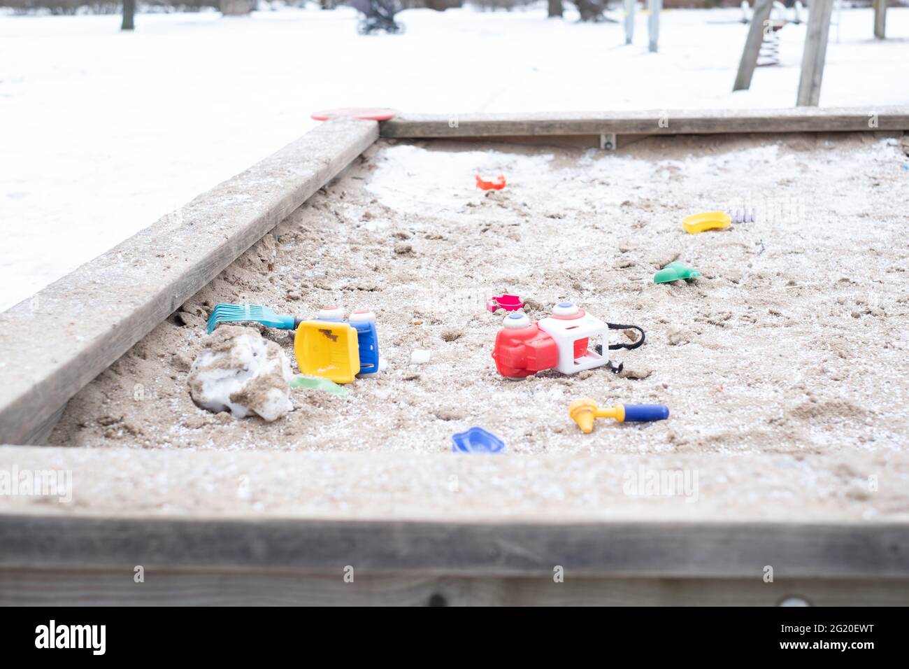 Kids toys scattered around in snowy frozen sandbox during winter lockdown. Stock Photo