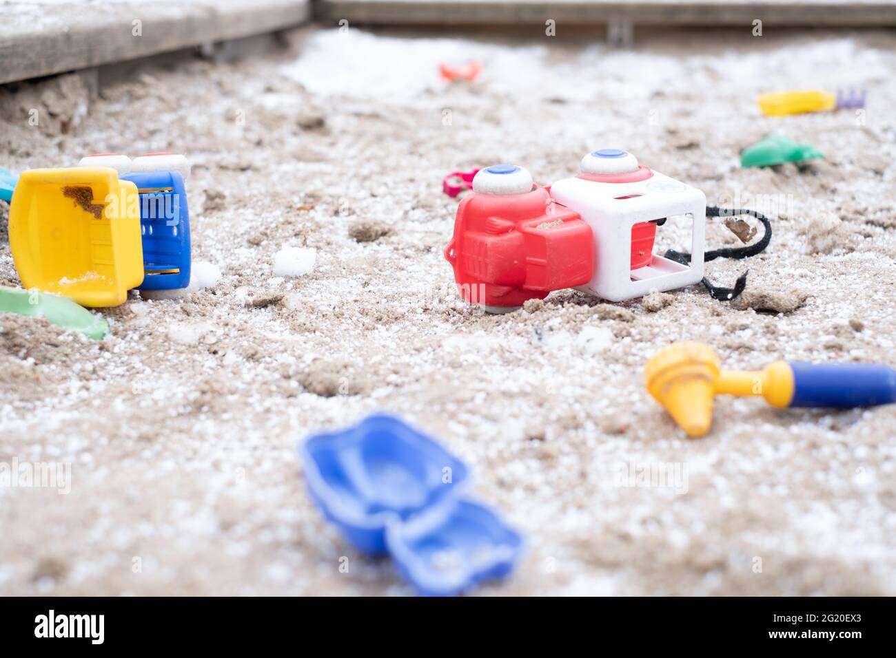 Kids toys scattered around in snowy frozen sandbox during winter lockdown. Stock Photo
