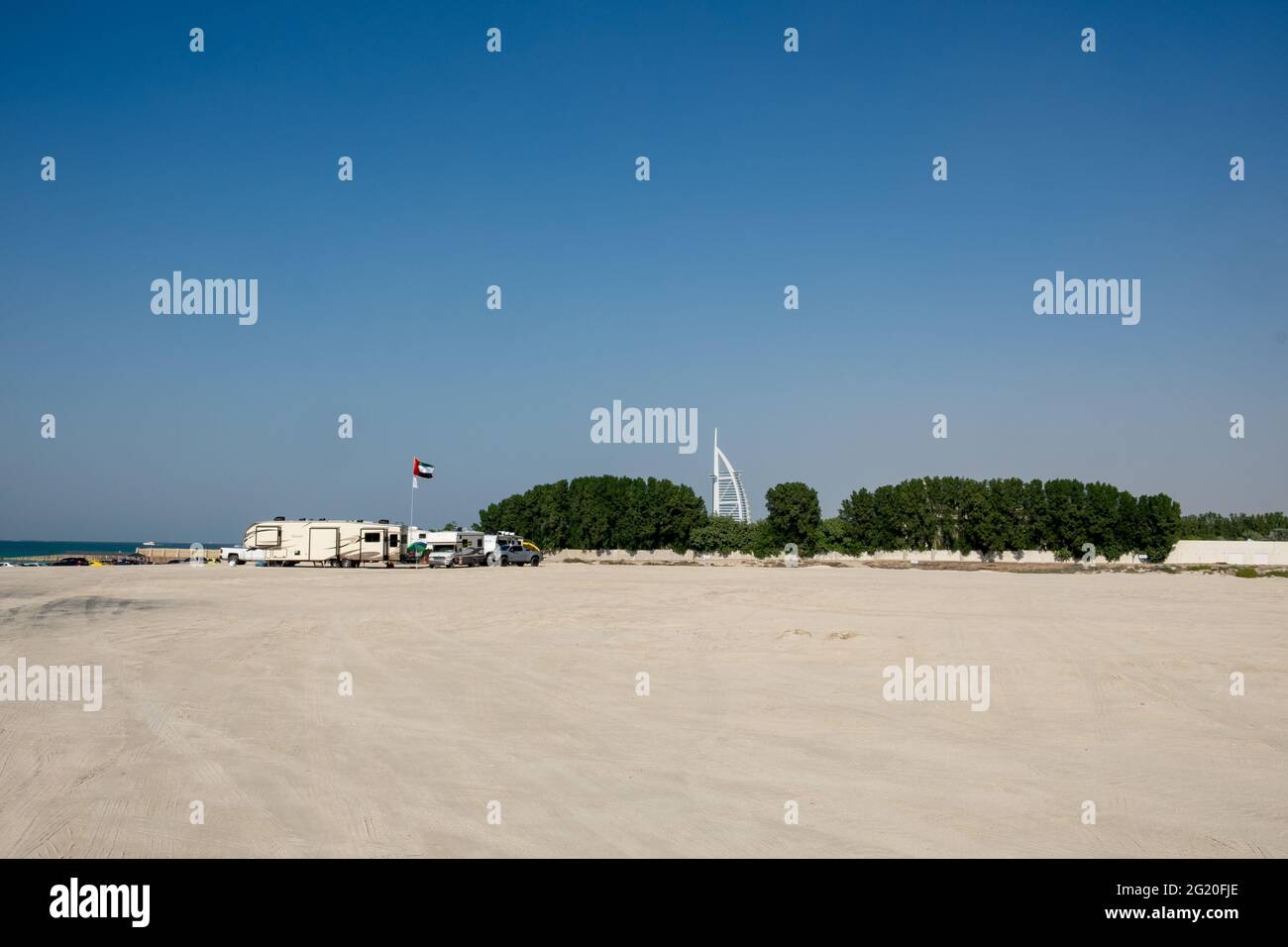 Campers on the beach with the white sail of Burj Al Arab visible in the distance. Dubai, UAE. Stock Photo