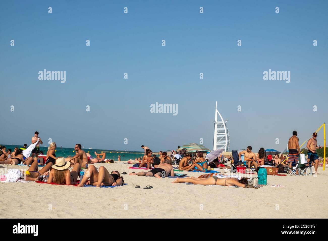People sunbathing on the beach in Dubai with the white sail ob Burj Al Arab in the background. Dubai, UAE. Stock Photo