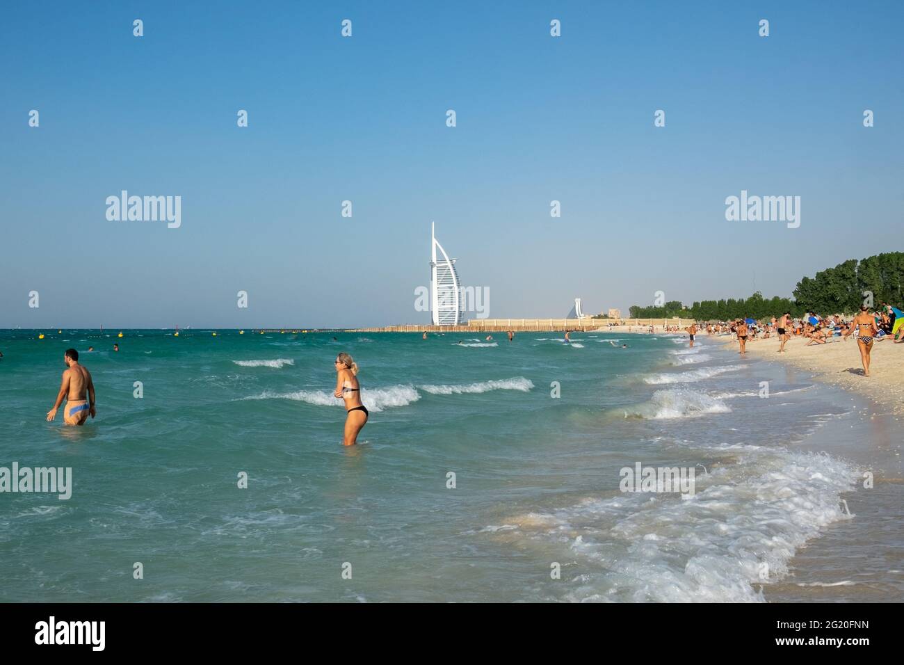 People swimming in the sea with the white sail of Burj Al Arab visible in the distance. Dubai, Stock Photo