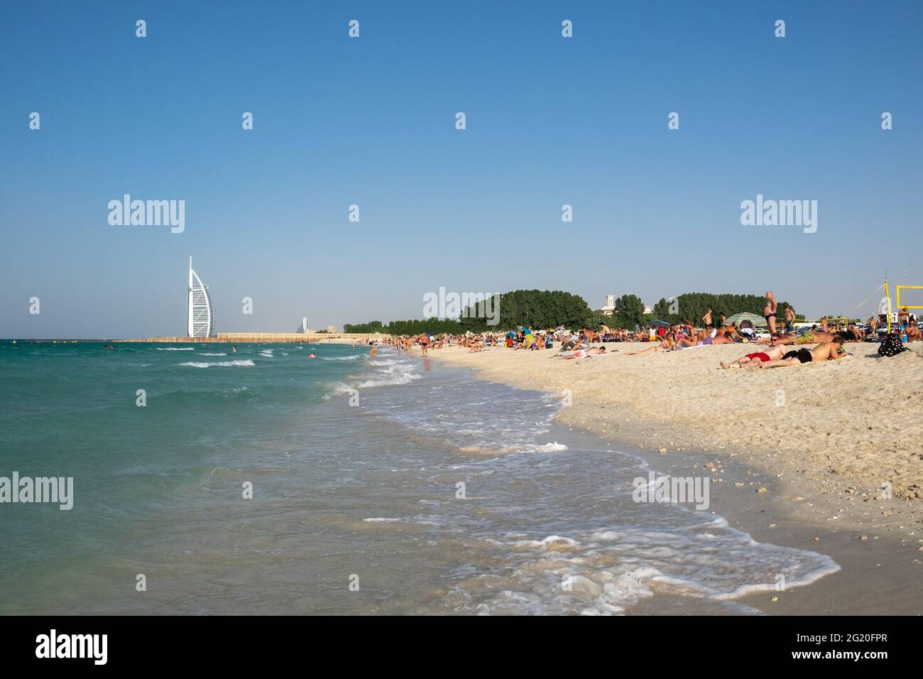 People sunbathing on the beach in Dubai with the white sail of Burj Al Arab in the background. Dubai, UAE. Stock Photo