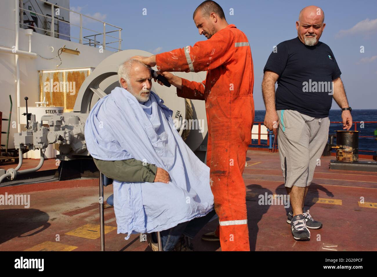 Able seaman is cutting masters hair. Sunday is the holiday even vessel is sailing in the middle of the ocean. Only, the afterpart barbershop is open but the barber is an able seaman. Stock Photo