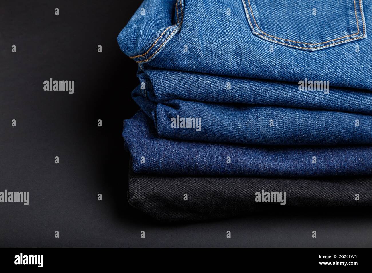 Blue jeans trousers stack. Stack of blue jeans on black background with copy space. Stock Photo
