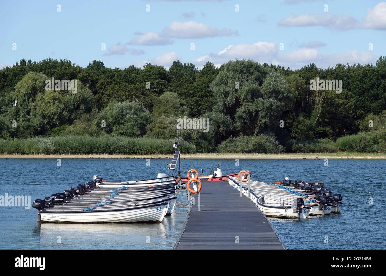 HANNINGFIELD, UNITED KINGDOM - Aug 03, 2020: Two rows of motor boats tied to a jetty on Hanningfield Reservoir in Essex with a wooded area in the back Stock Photo