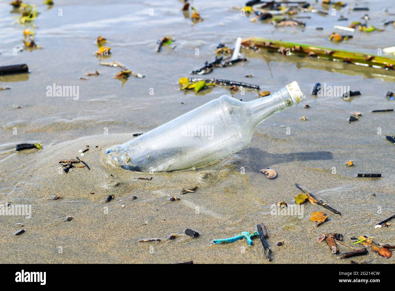 Glass water bottle pollution in ocean (Environment concept). Ocean pollution: waste on the beach. Stock Photo