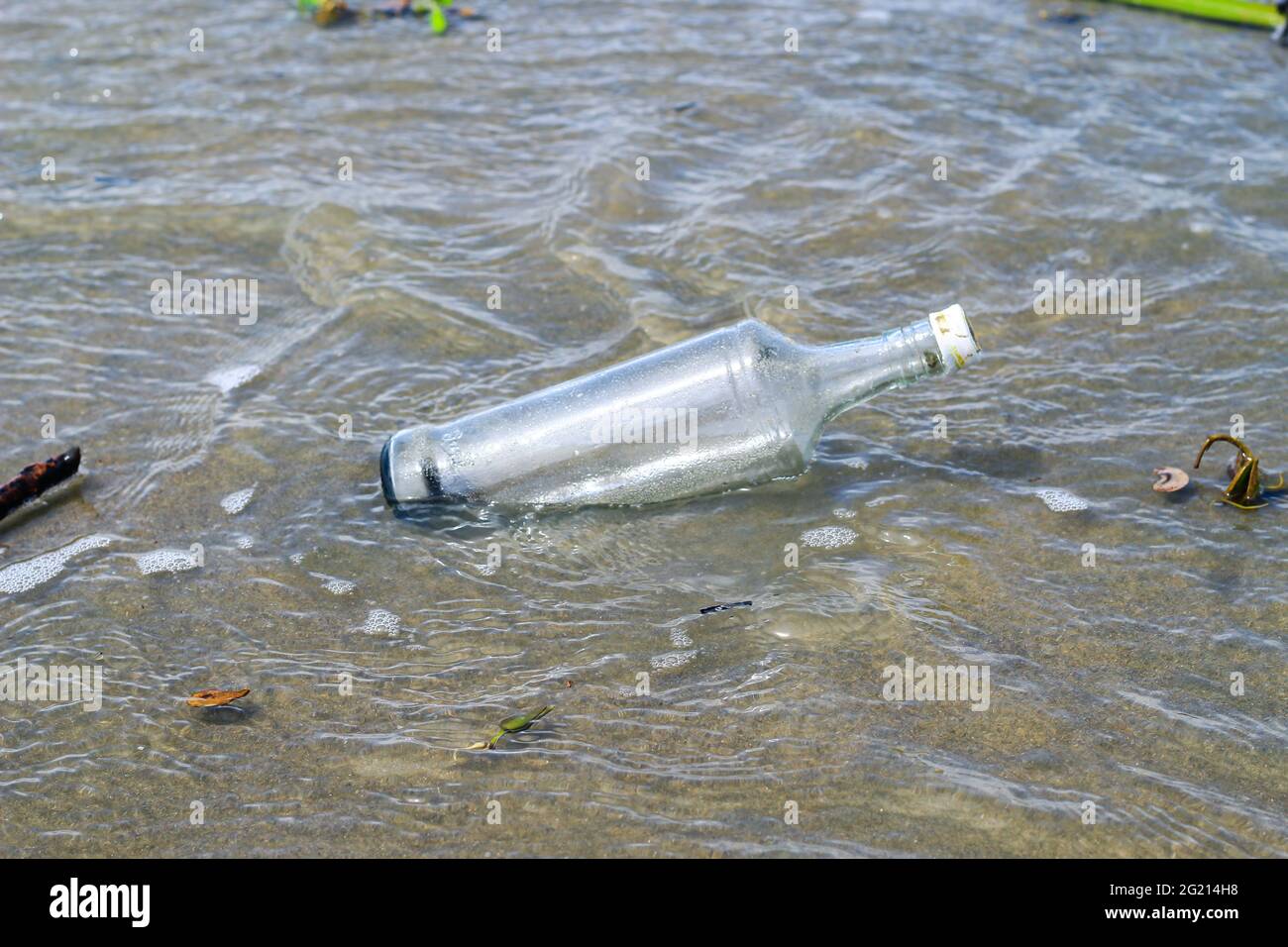 Glass water bottle pollution in ocean (Environment concept). Ocean pollution: waste on the beach. Stock Photo
