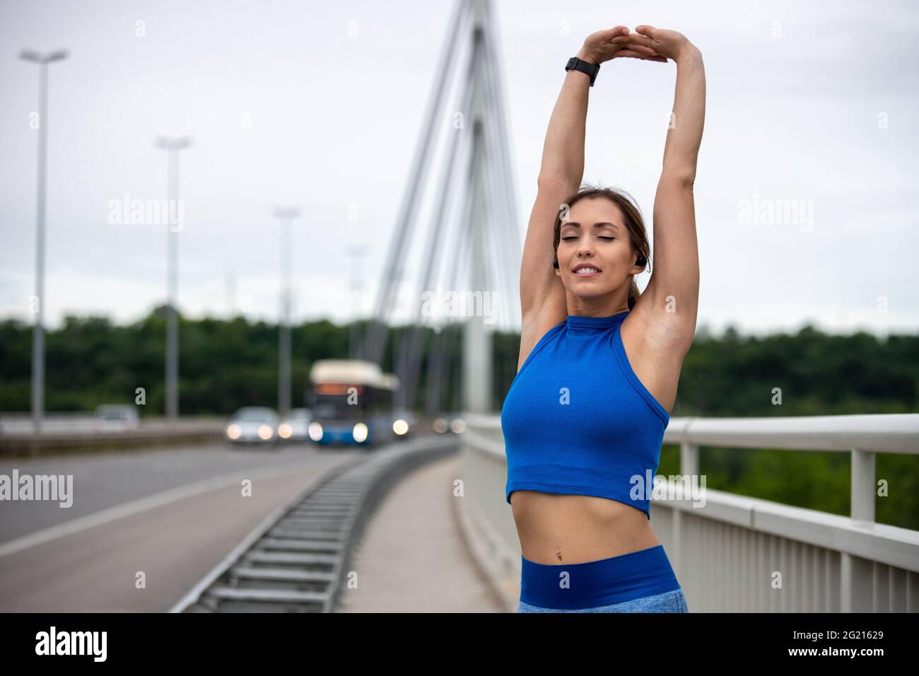 Young woman standing on bridge stretching arms overhead. Flexible