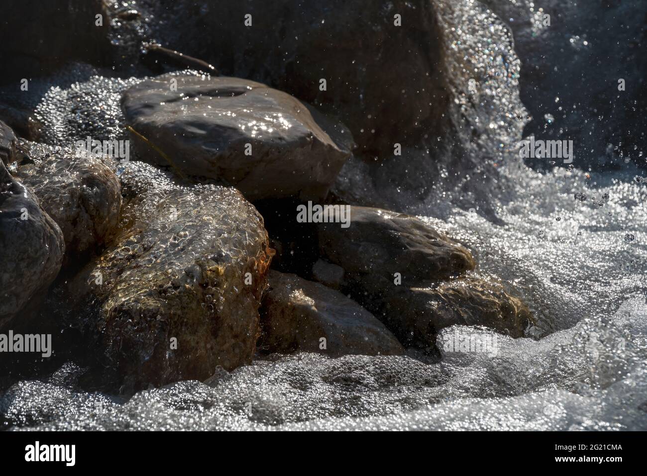 The chaos of a fresh clear mountain creek flowing over sunny rocks while splashing water drops and creating bubbles, Tirol, Austria Stock Photo