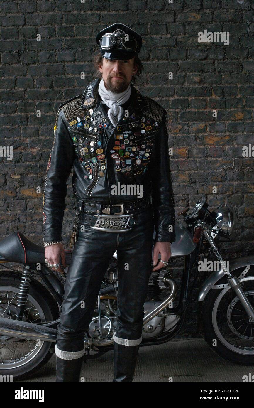 Rocker in cafe racer gear wearing black leather jacket covered in studs, patches and badges classic british motorcycle in London , UK Stock Photo