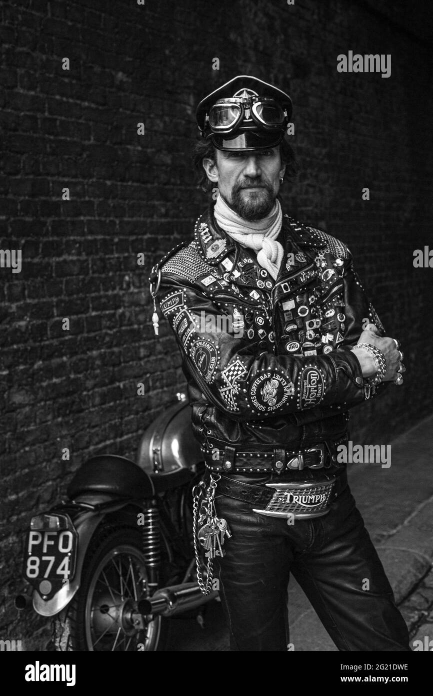 Rocker in cafe racer gear wearing black leather jacket covered in studs, patches and badges classic british motorcycle in London , UK Stock Photo