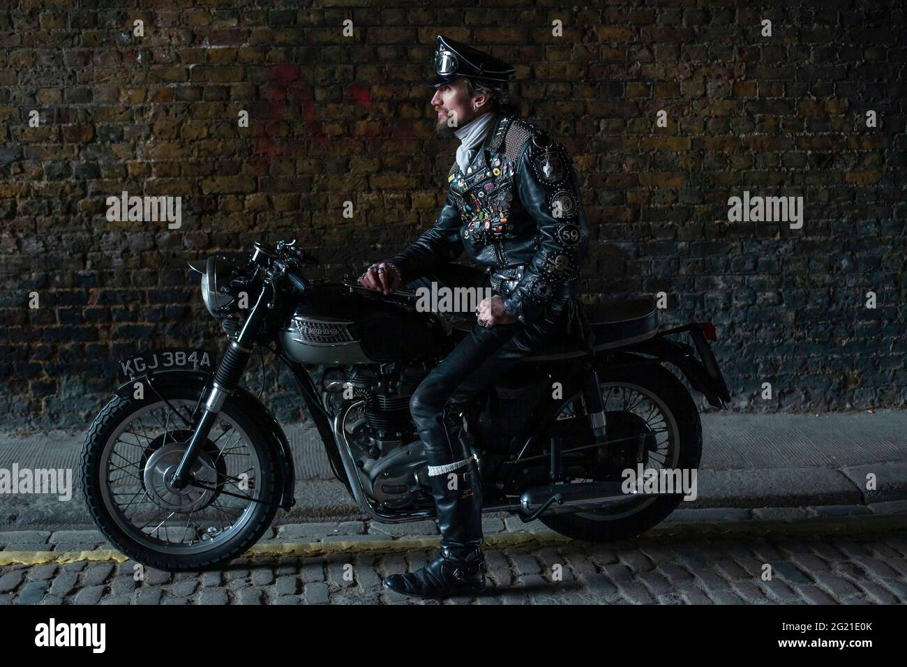 Rocker in cafe racer gear wearing black leather jacket covered in studs, patches and badges classic british motorcycle in London , UK Stock Photo