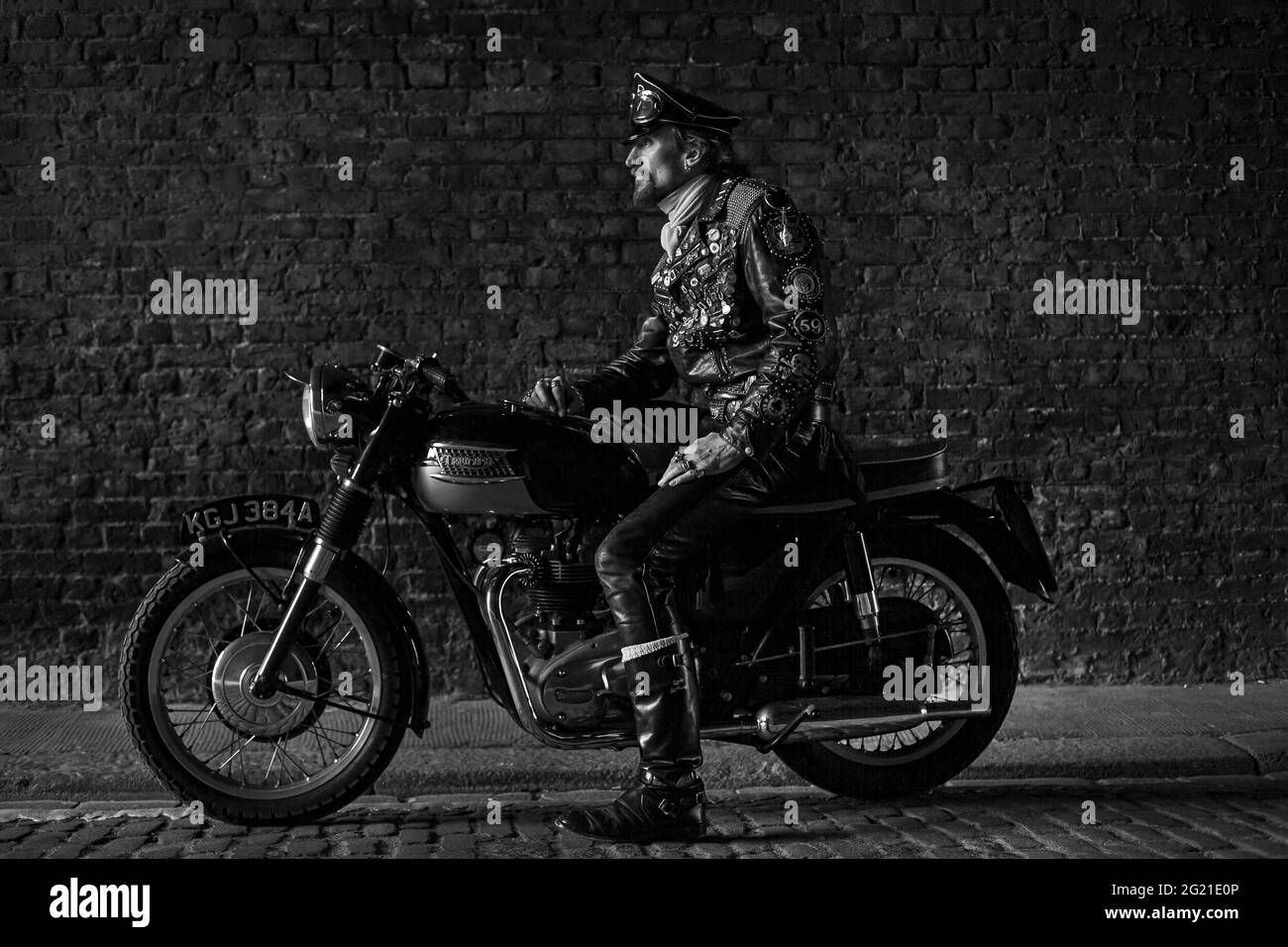 Rocker in cafe racer gear wearing black leather jacket covered in studs, patches and badges classic british motorcycle in London , UK Stock Photo