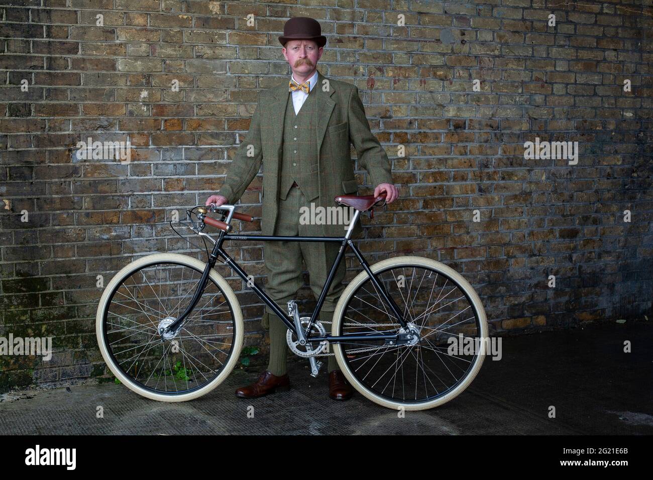 London a elegant man standing beside Pashley Guvnor bike wearing suit with bowler hat and bow tie . Stock Photo