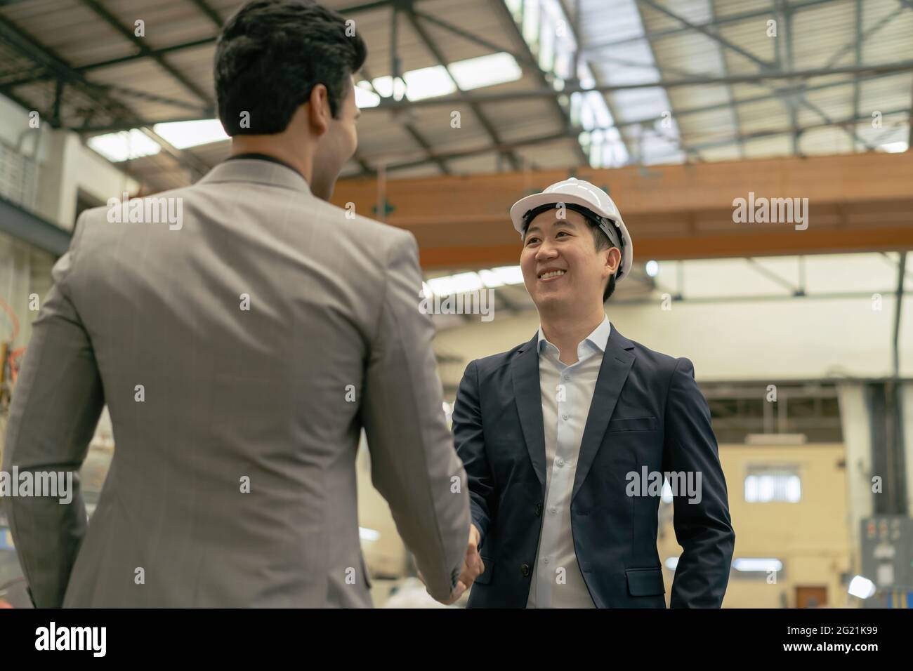 30s young Asian businessman in formal suit and hard hat showing foreign business partner in factory background. Business partnership and team work success concept - 4K Real Time Footage Stock Photo