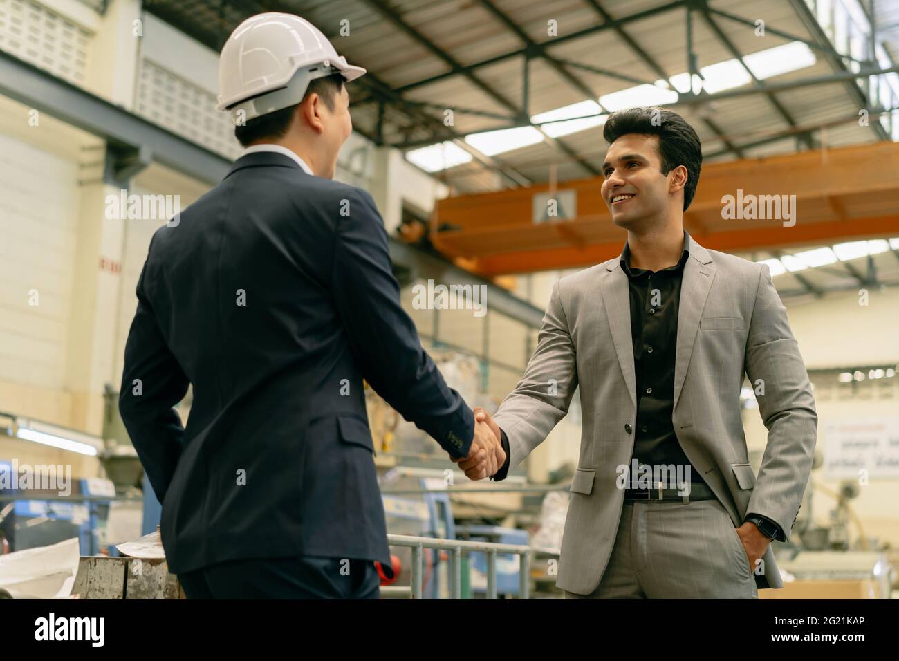 30s young Asian businessman in formal suit and hard hat showing foreign business partner in factory background. Business partnership and team work success concept - 4K Real Time Footage Stock Photo