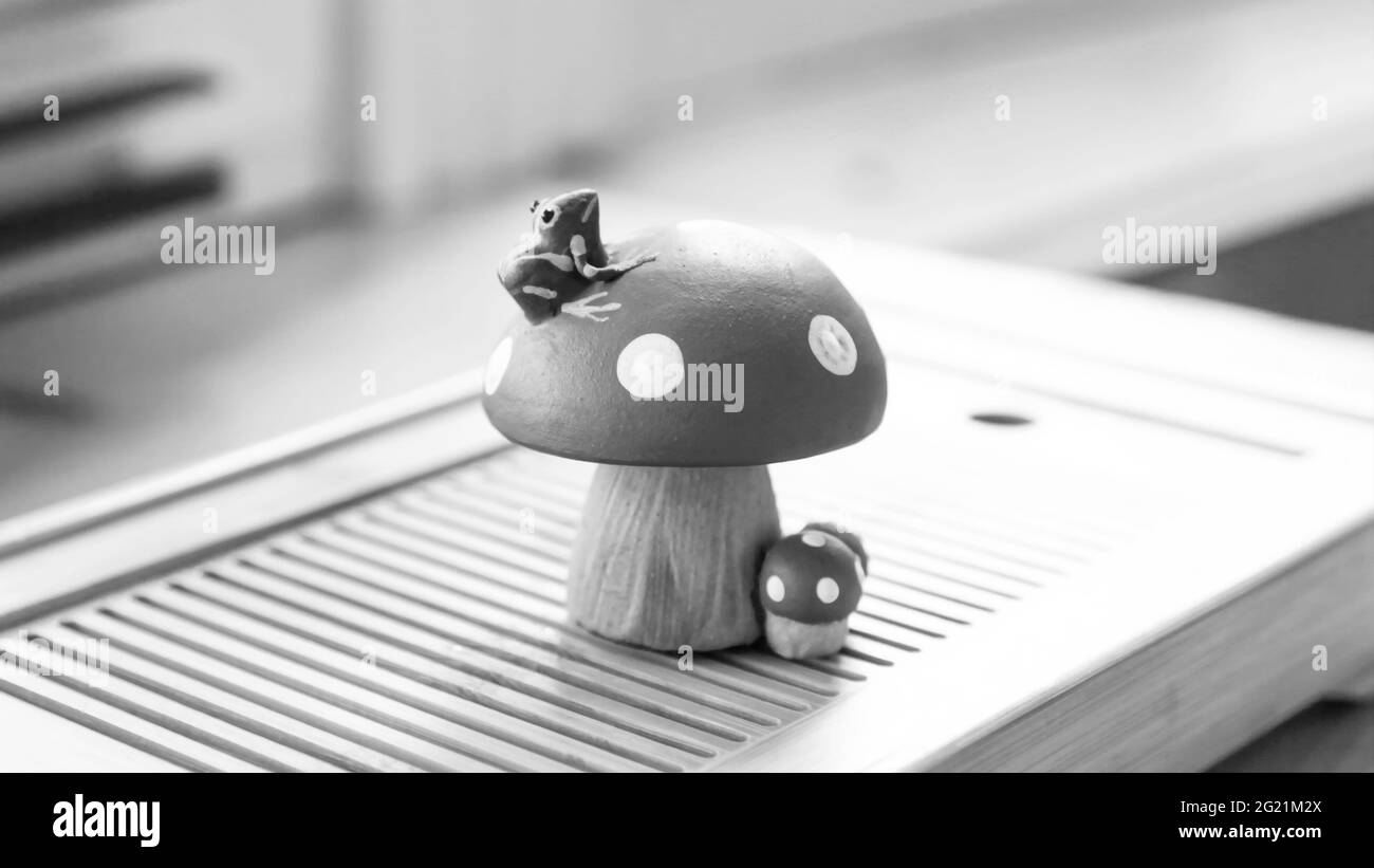 A small frog sitting on a fly agaric. Clay tea figurine, teapet. Black and white photo. Stock Photo