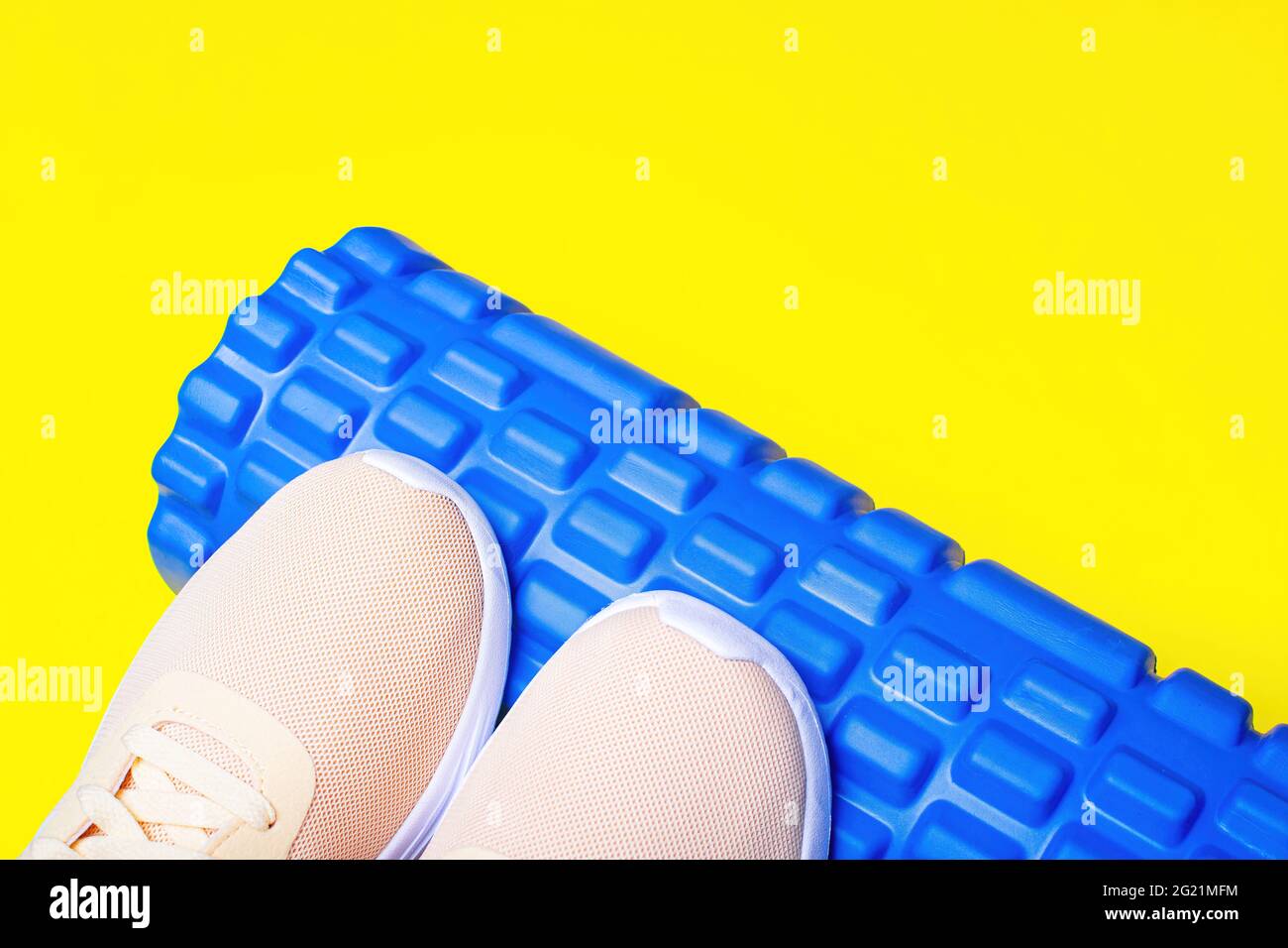 Peach sneakers and foam massage roller on yellow background. Massage roll for relieving tension in the legs. Stock Photo
