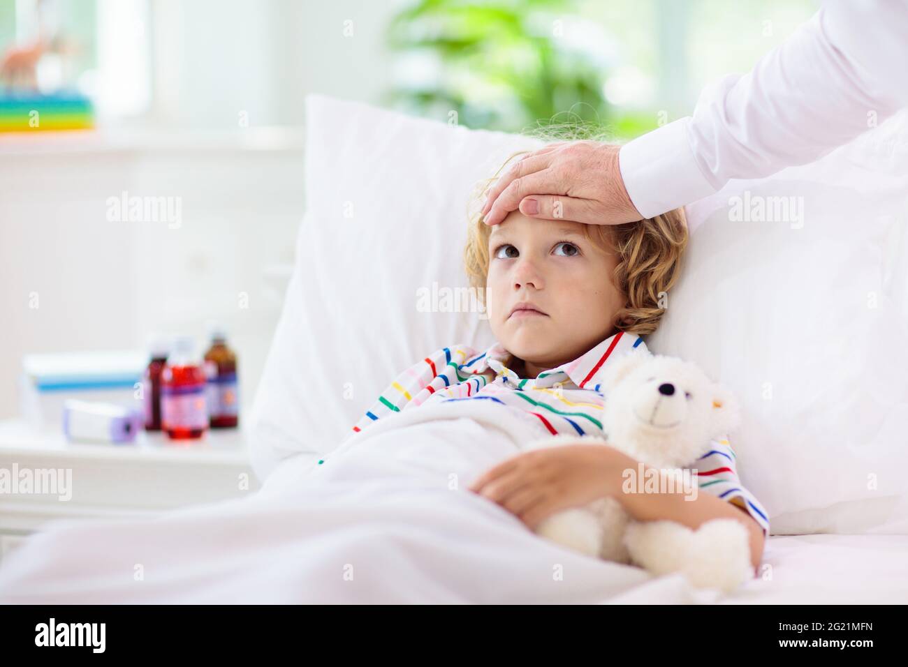 Sick little boy with medicine. Mother checking fever of ill child in bed. Unwell kid with chamber inhaler for asthma cough treatment. Flu season. Stock Photo