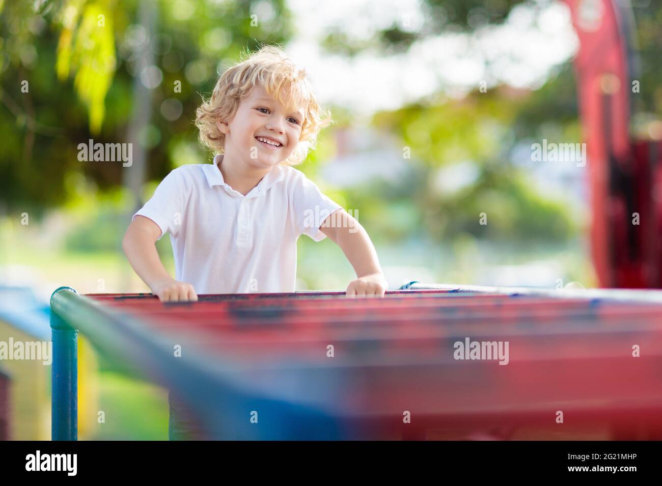 Child playing on outdoor playground in rain. Kids play on school or kindergarten yard. Active kid on colorful monkey bars. Healthy summer activity Stock Photo