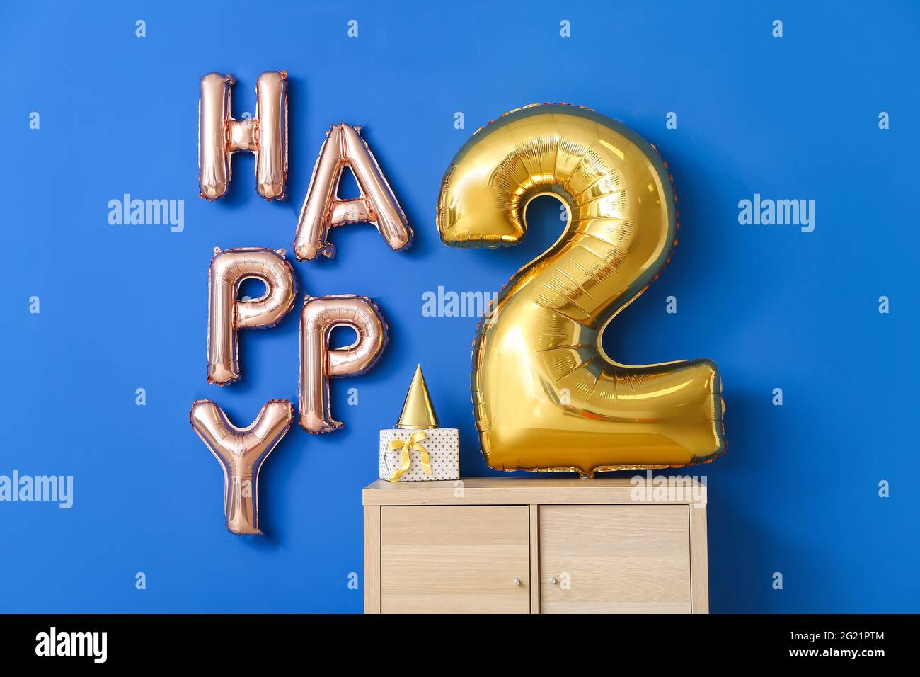 Text HAPPY 2 made of air balloons and chest of drawers near color wall Stock Photo