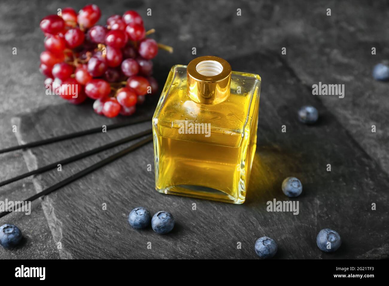 Reed diffuser with grapes and blueberries on dark background Stock Photo
