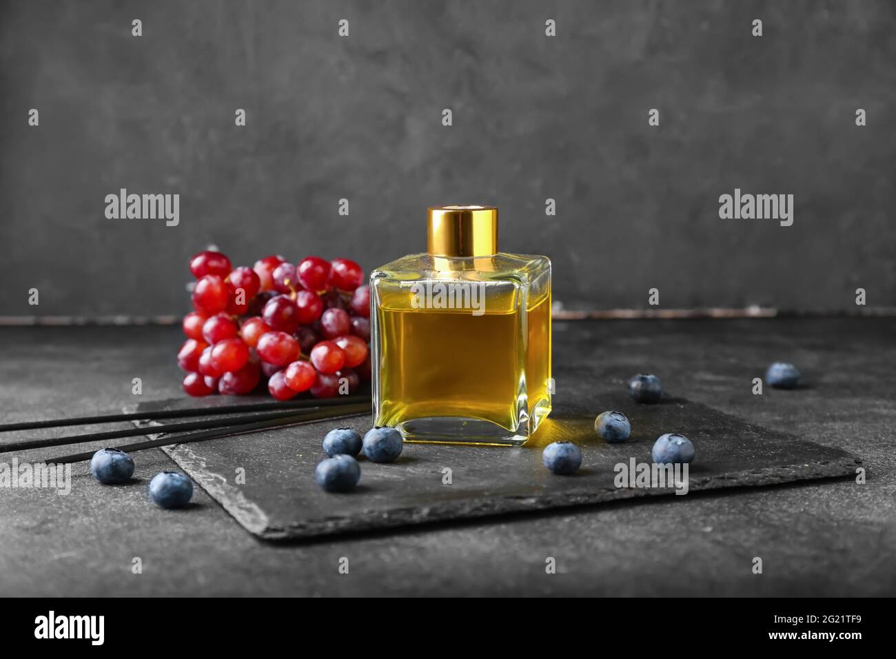 Reed diffuser with grapes and blueberries on dark background Stock Photo