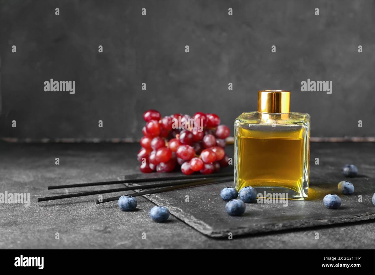 Reed diffuser with grapes and blueberries on dark background Stock Photo