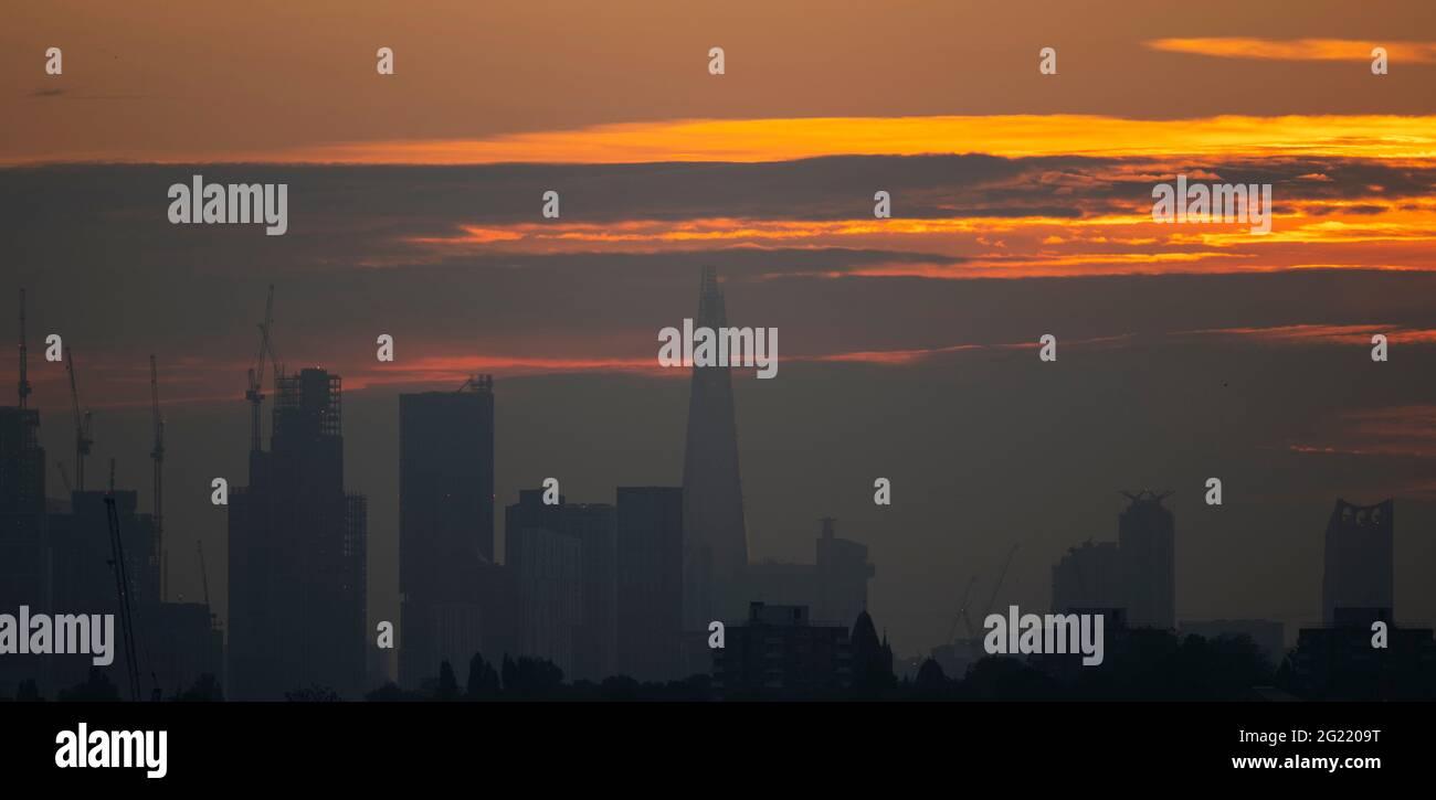 London, UK. 8 June 2021. Colourful cloudy sky lit by the rising sun behind London skyscrapers, seen from Wimbledon. Credit: Malcolm Park/Alamy Live News. Stock Photo