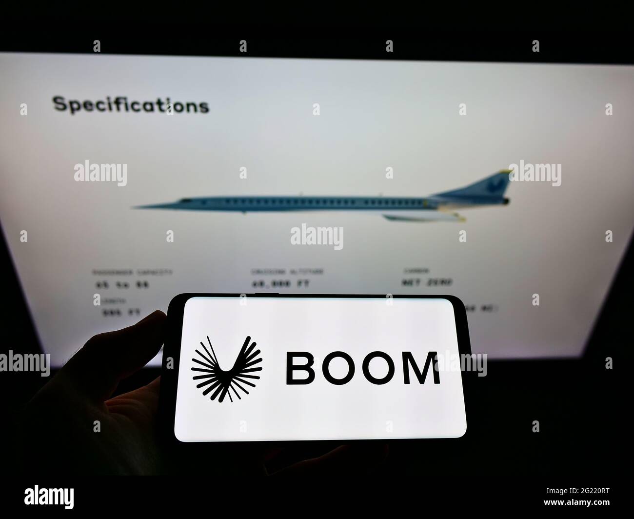 Person holding cellphone with logo of US aerospace company Boom Technology Inc. (Supersonic) on screen in front of web page. Focus on phone display. Stock Photo