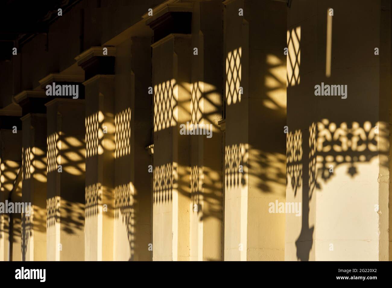 Detail of early morning shadows made by fancy cast iron lace on the walls of an old painted sandstone building. Stock Photo