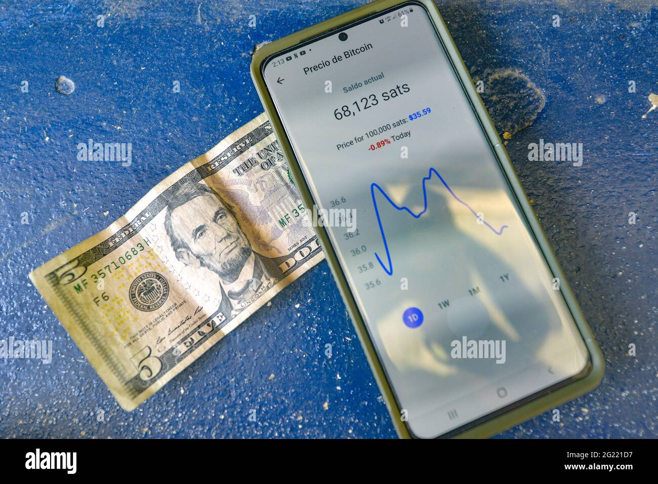 A five US Dollar bill is seen next to a phone displaying an application  used to transfer Bitcoin. Salvadoran President Nayib Bukele has announced  that he will propose a law to the