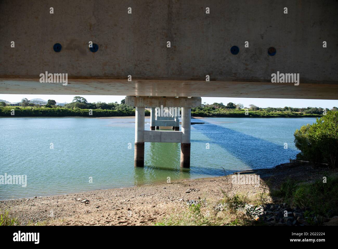 The underside of a new reinforced concrete bridge across a river showing pylons and beams reducing in size with copy space Stock Photo