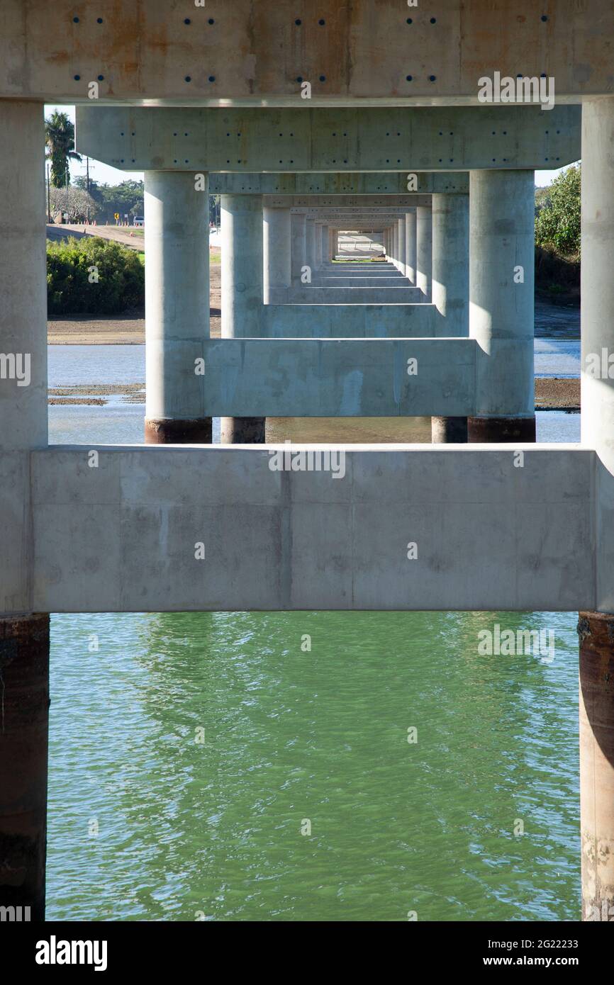 The underside of a new reinforced concrete bridge across a river showing pylons and beams reducing in size. Stock Photo