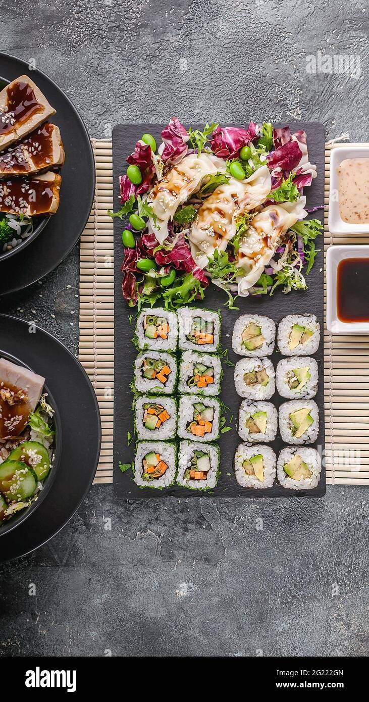 https://c8.alamy.com/comp/2G222GN/mix-of-asian-dishes-vegetable-sushi-maki-rolls-gyoza-dumplings-with-salad-on-a-black-stone-board-pork-and-chicken-dishes-in-bowls-bamboo-mat-nut-2G222GN.jpg