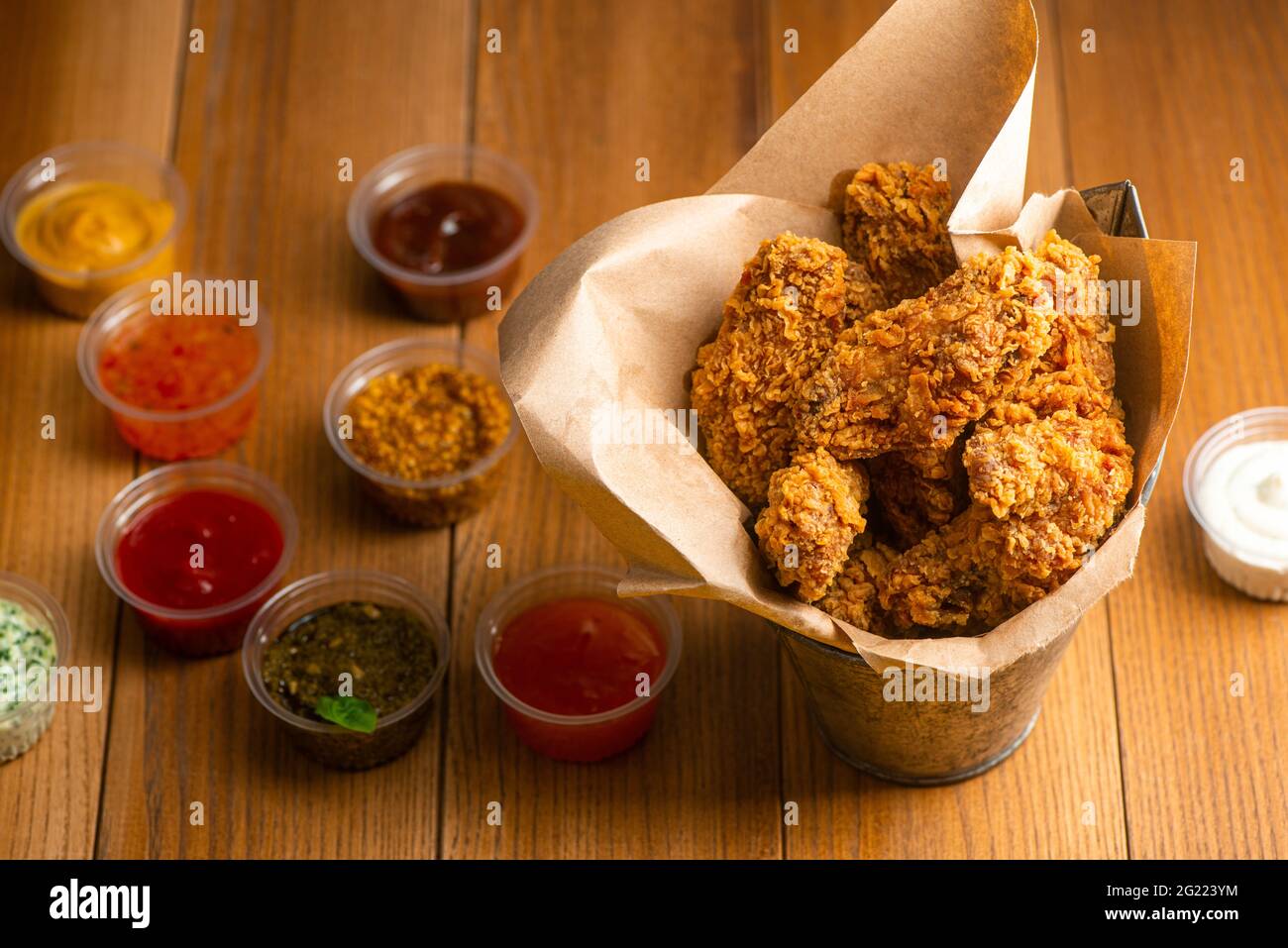 Bucket of chicken wings served with cups of different sauces on wooden table Stock Photo