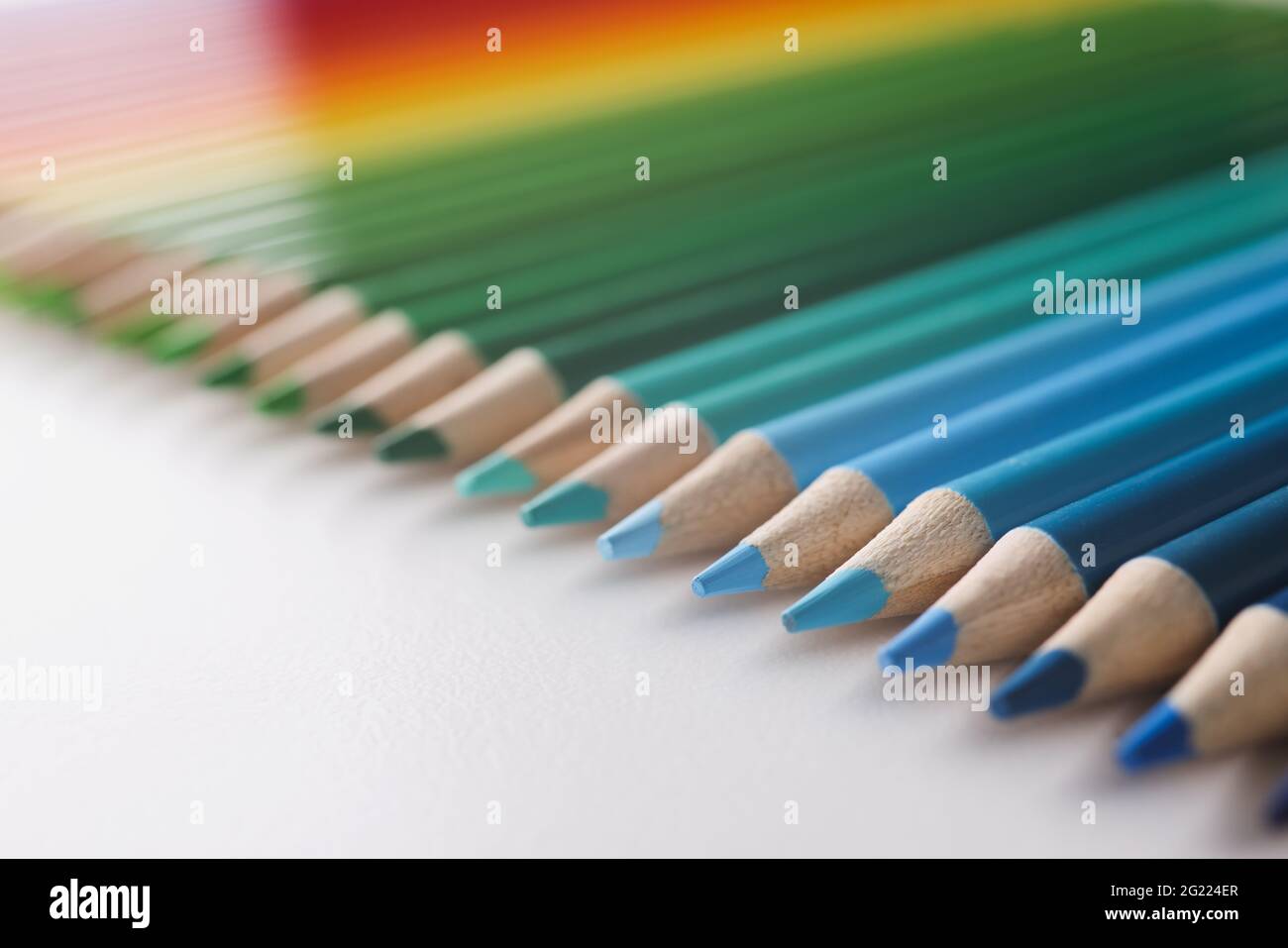 Many multi-colored pencils lying in colors of rainbow on white ...
