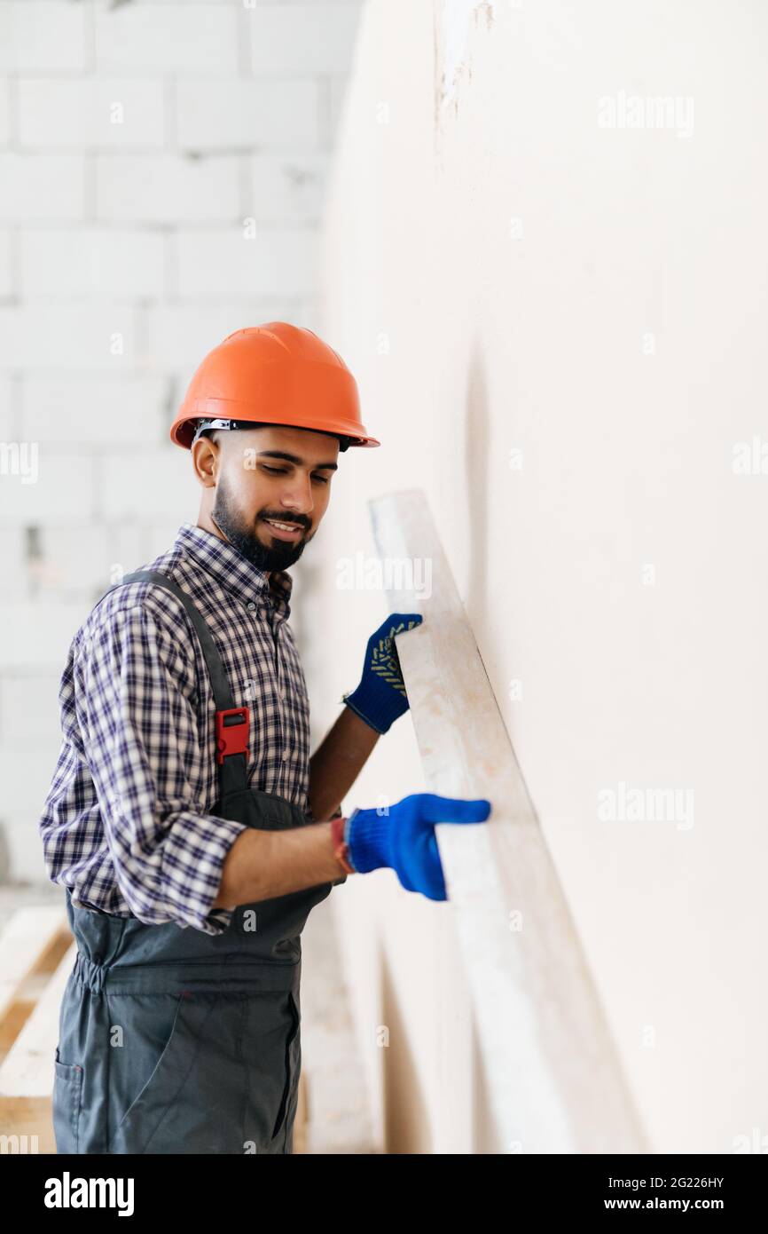 A worker in cap, holding a comb putty knife and covering a wall surface